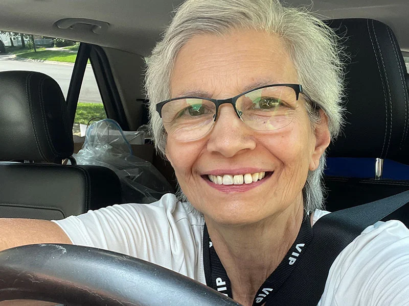 A woman with glasses sitting in the driver 's seat of a car.