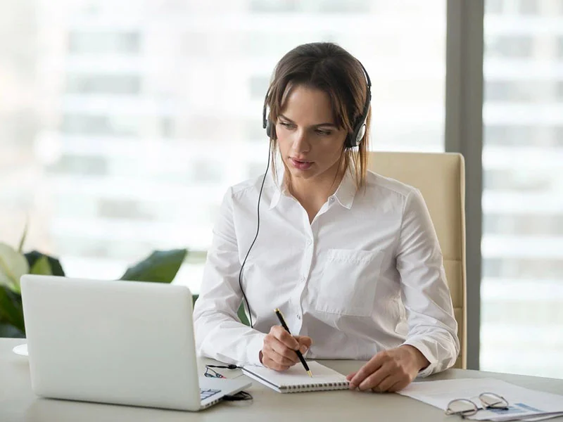 A woman with headphones on sitting at her desk.